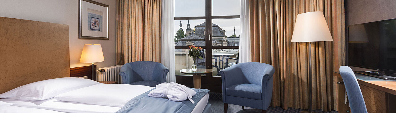 Elegant superior room at Maritim Hotel Fulda with double bed, seating area, and balcony overlooking the city.