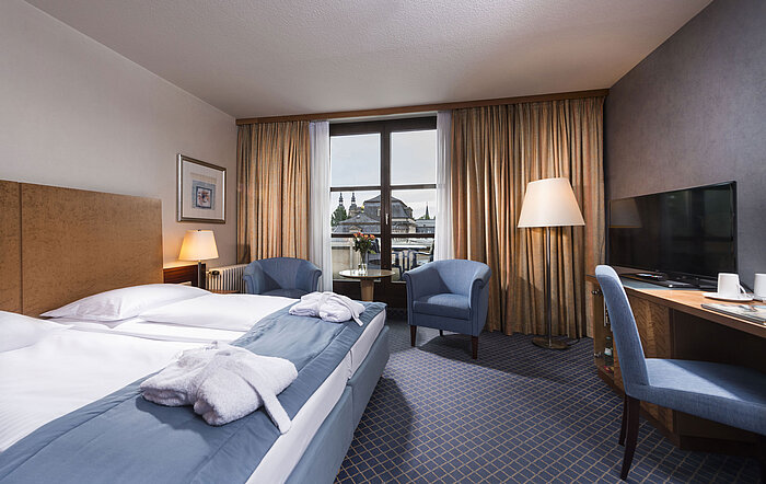 Elegant superior room at Maritim Hotel Fulda with double bed, seating area, and balcony overlooking the city.