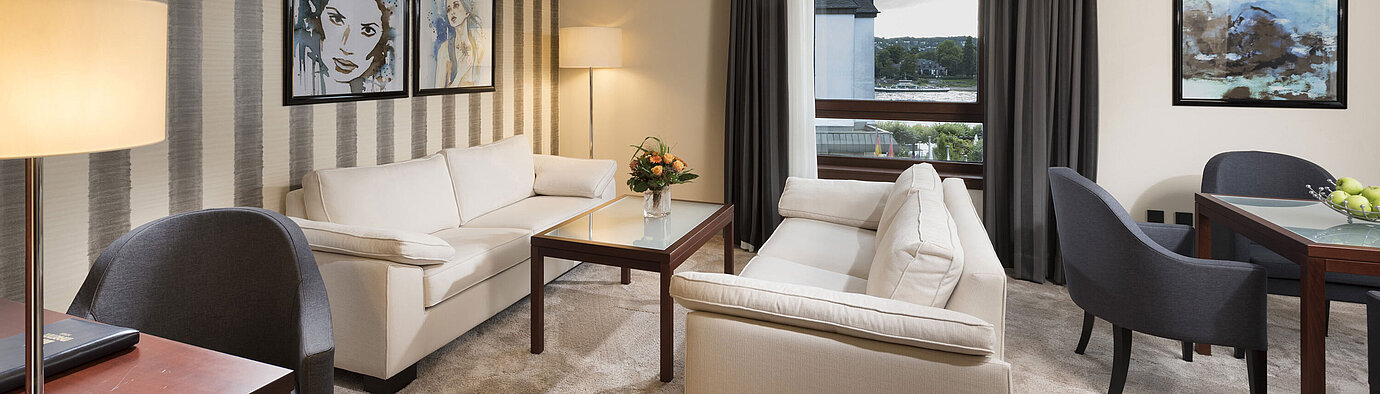Spacious suite with stylish sofas, dining table, and panoramic Rhine view at Maritim Hotel Königswinter.