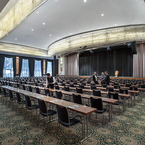 Magnificent hall at the Maritim Hotel Magdeburg with a stage, row seating, and luxurious chandelier.