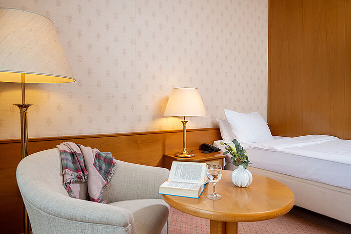 Superior Single room Cosy seating area with armchair, table, lamp and a view of the single bed in the hotel room.
