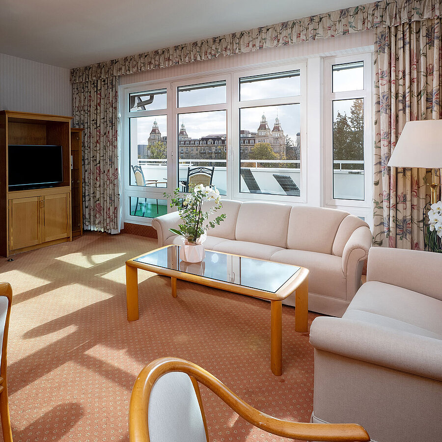 Junior Suite with bright living area, sofa, large window, dining space and classic interior at the Maritim Hotel.