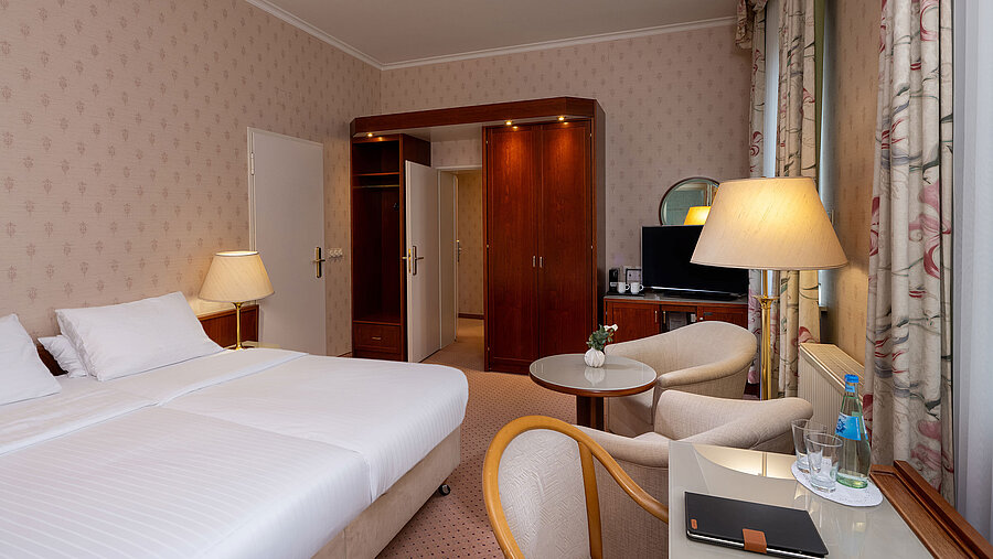 Comfort family room with double bed, seating area, desk, TV and bright, cosy interior.