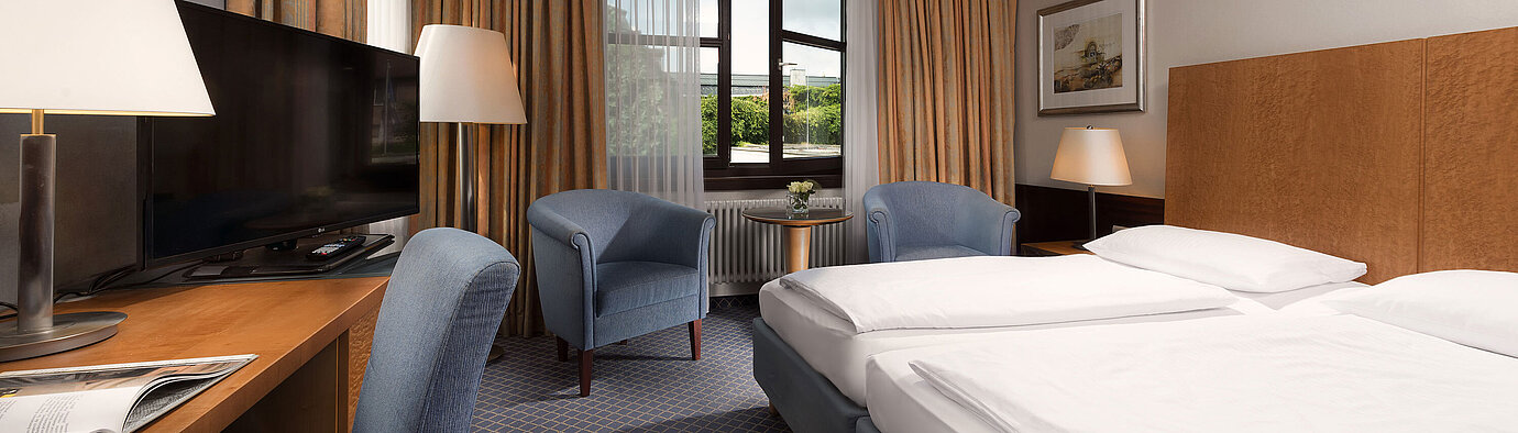 Classic room at Maritim Hotel Fulda with a cozy double bed, desk, seating area, and large window.