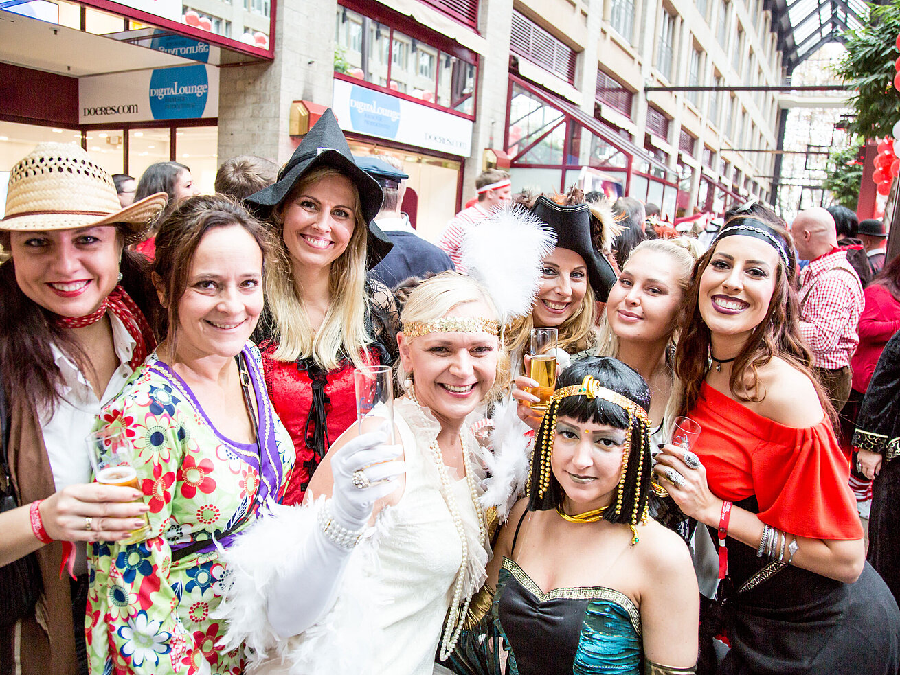 carnival Women in colorful costumes celebrate at a carnival and hold champagne glasses up to the camera.