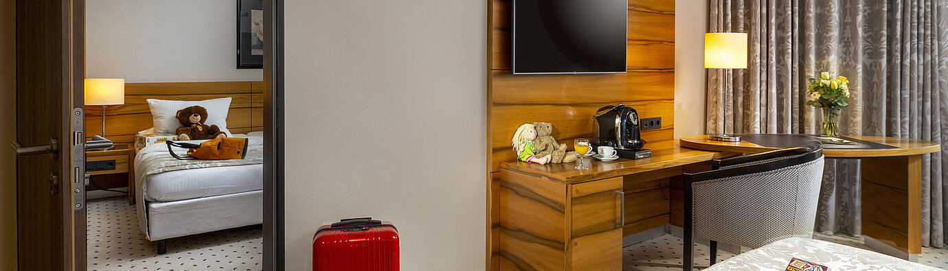 Family room at Maritim Hotel Bad Homburg with separate kids' room, teddy bears, and red suitcase.