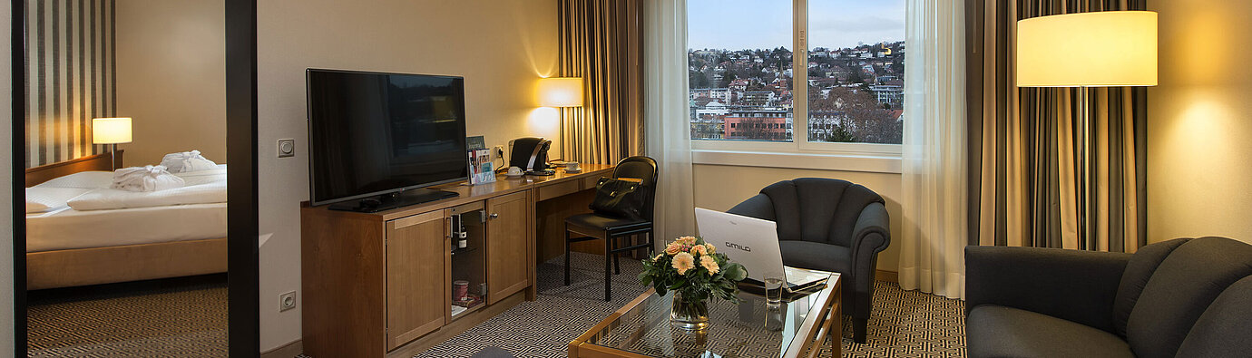 Junior suite Living area with sofa, TV, desk and city view in the suite at the Maritim Hotel Stuttgart