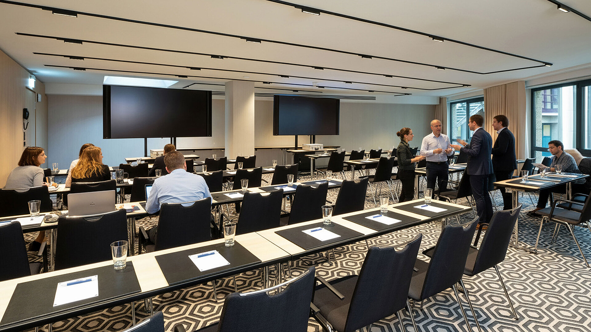 Meeting room 1 with theatre-style seating, participants in discussion, multiple screens and modern media technology.