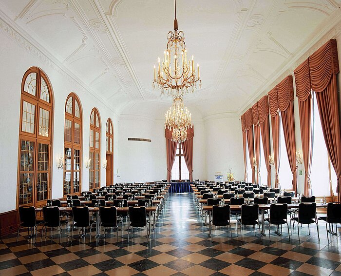 Elegant event hall at Maritim Hotel Fulda with chandeliers, high windows, and stylish seating for events.