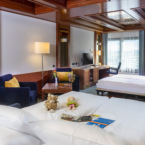 Family room at Maritim Hotel Darmstadt with toys on the bed, a desk with TV, and a cozy seating area.
