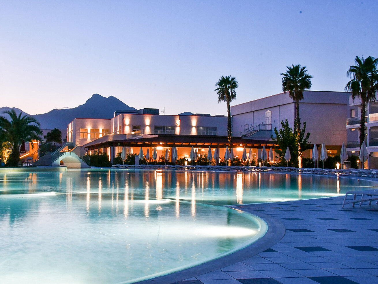 Pool Evening lights at the pool of Maritim Resort Calabria with palm trees and mountain backdrop