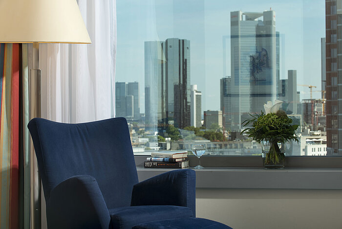 View of the skyline of Frankfurt  View from a suite at Maritim Hotel Frankfurt with skyline view, blue armchair, and decorative flower arrangement.