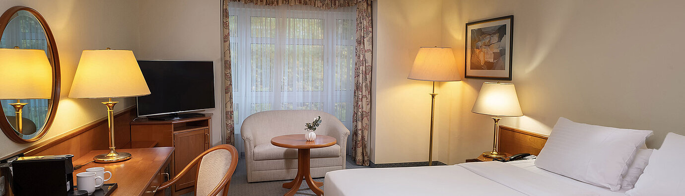 Classic room Classic room with double bed, desk, TV, seating area and large window in a bright interior design.