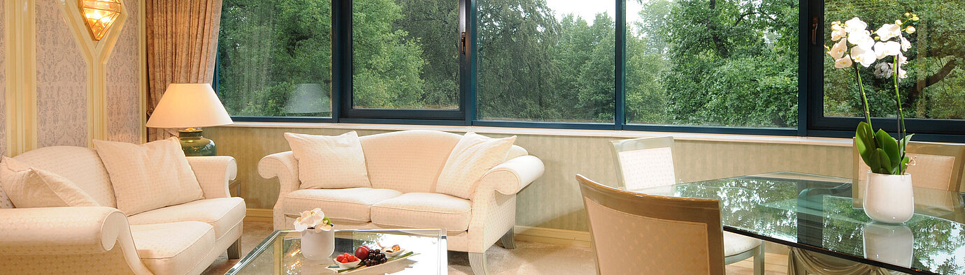 Suite  Luxurious Suite with elegant seating, glass dining table, and large panoramic window with greenery view.