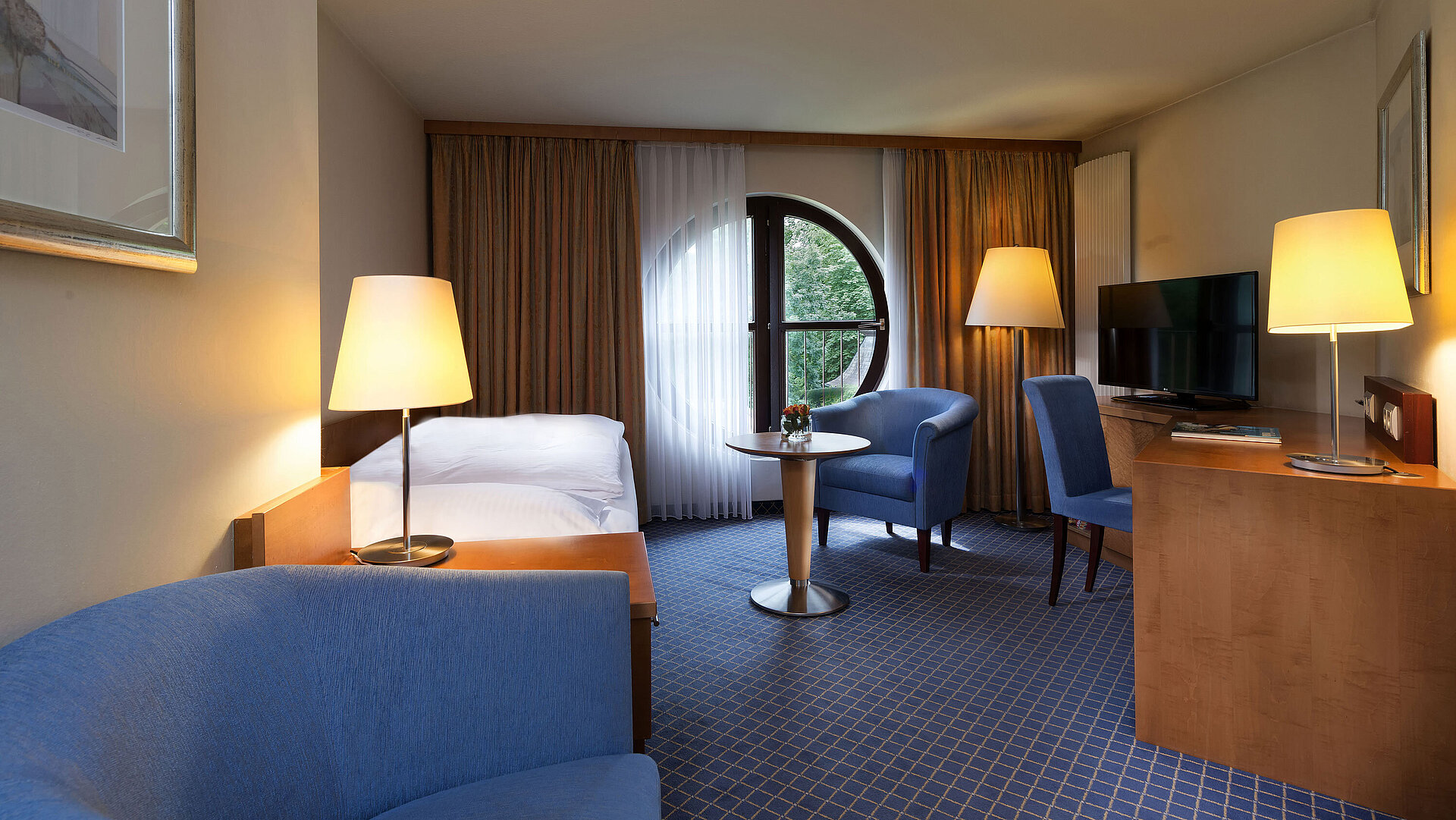 Classic room at Maritim Hotel Fulda with single bed, desk, seating area, and round window with a view.