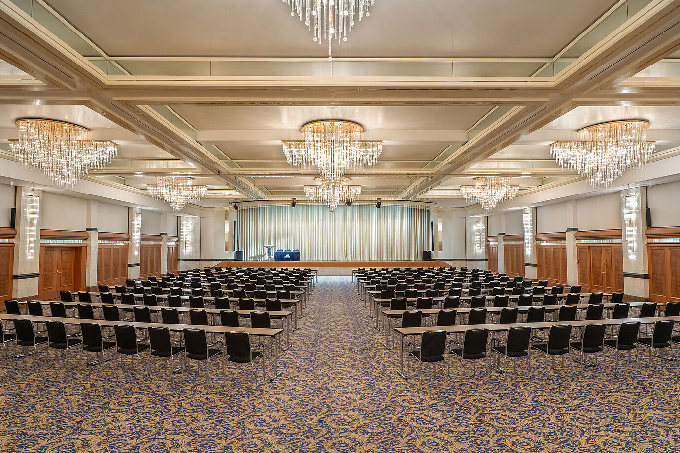 Salle Fürst-von-Metternich avec grande scène, rangées de sièges, lustres élégants et ambiance lumineuse.
