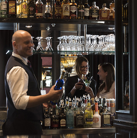 Happy guests enjoying cocktails at the bar of Maritim Hotel Dresden, served by a friendly bartender.