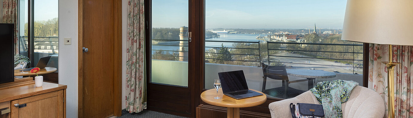 Bright hotel room with balcony, desk and view of the Trave River and Lübeck Bay