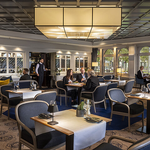 Elegant restaurant at Maritim Hotel Darmstadt with guests dining and relaxing. Modern decor and large windows with a view.