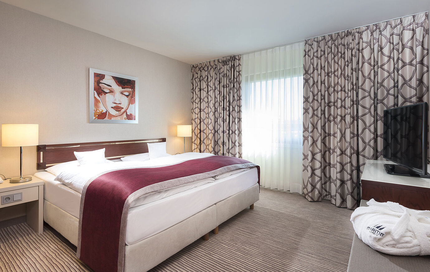 Spacious suite at Maritim Hotel Bonn with a cozy double bed, modern decor, and a wine-red bed runner.