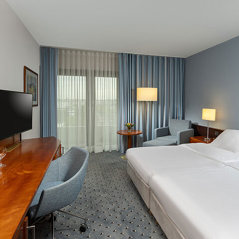 Classic double room at Maritim Hotel Darmstadt with desk, flat-screen TV, seating area, and large windows with curtains.
