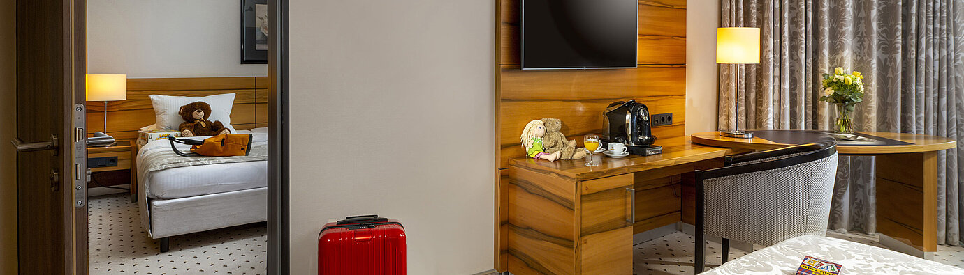 Family room at Maritim Hotel Bad Homburg with separate kids' room, red suitcase, and teddy bear.