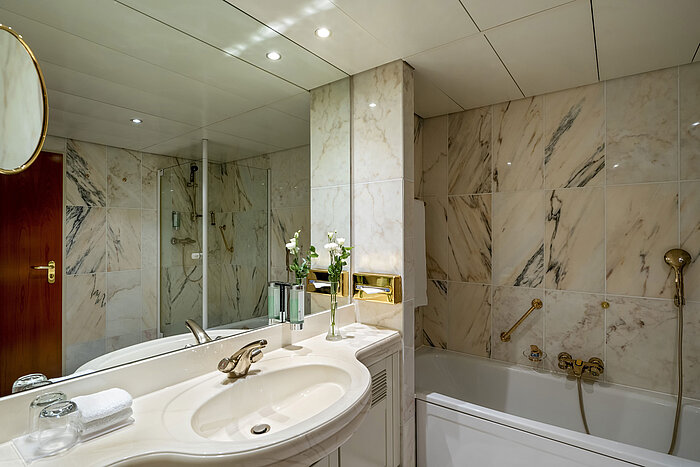 Master Suite Modern bathroom at Maritim Hotel Hannover with bathtub, glass shower, and marble walls.