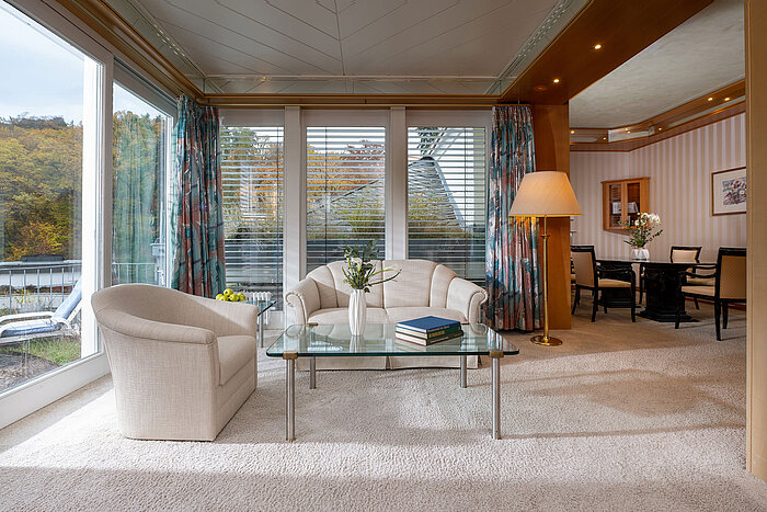 Wintergarden Suite Bright hotel suite living area with glass table, cosy armchairs and large windows offering a view.
