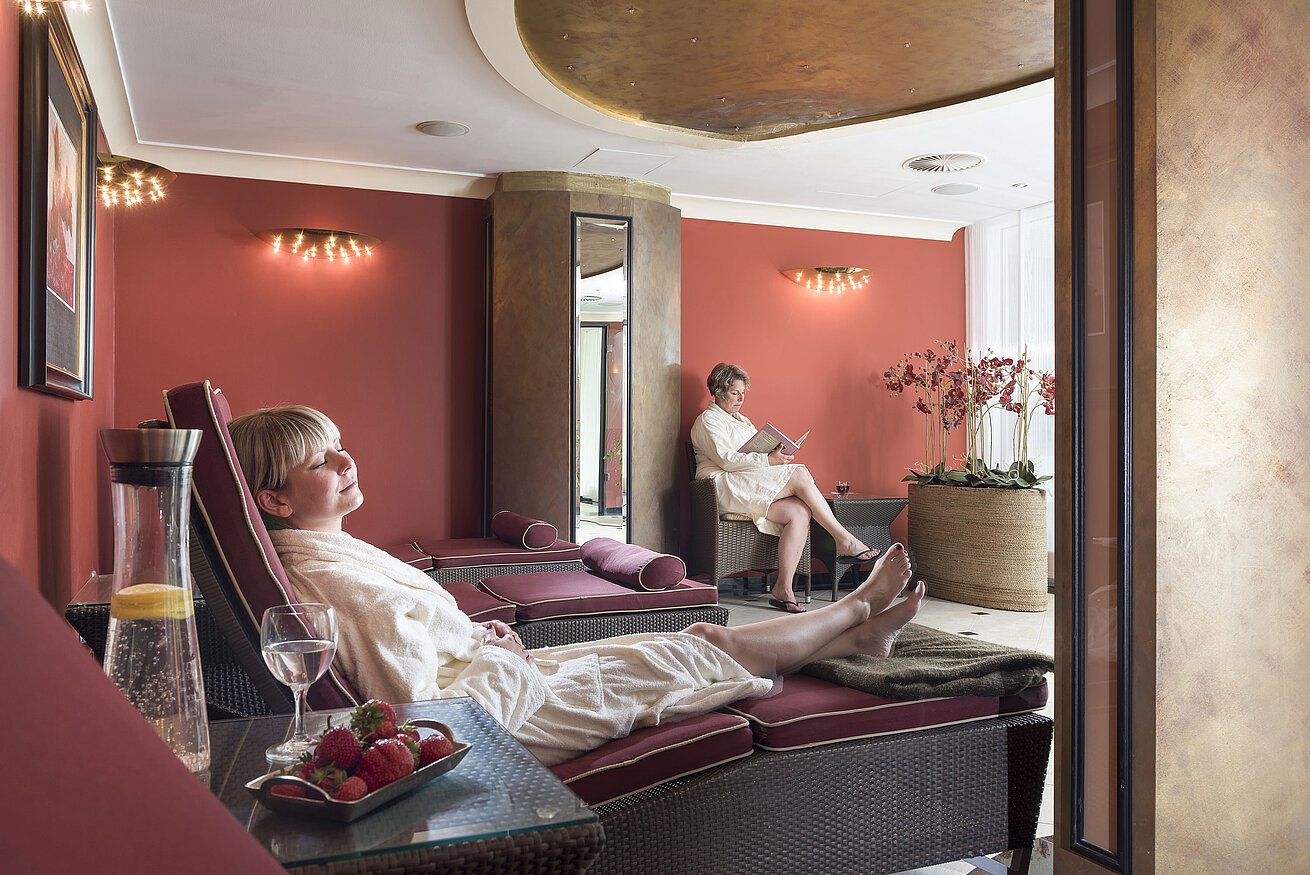 Relaxation room with red walls at Maritim Seehotel Timmendorfer Strand, guests relaxing on loungers.