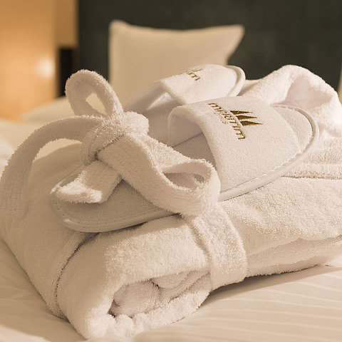 A fluffy bathrobe and slippers with Maritim logo on a bed at the Maritim proArte Hotel Berlin.