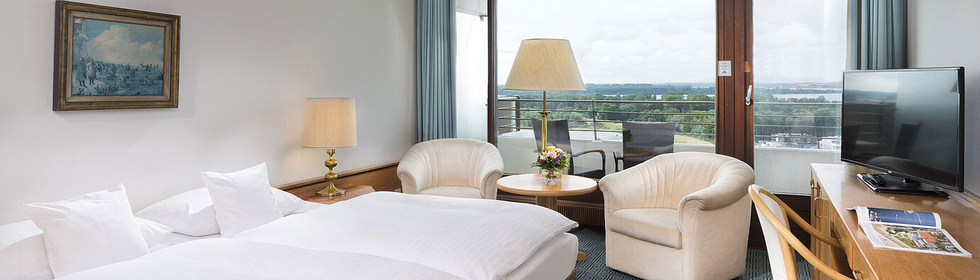 Double room with seating area, desk and balcony overlooking green landscape in Travemünde